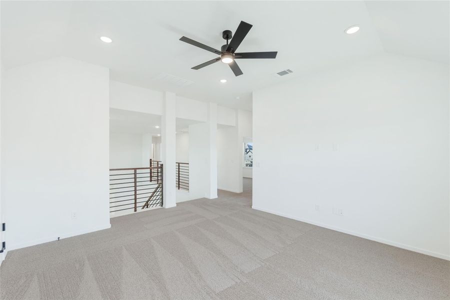 Open upstairs living area with carpet, ceiling fan, and metal railing overlooking staircase