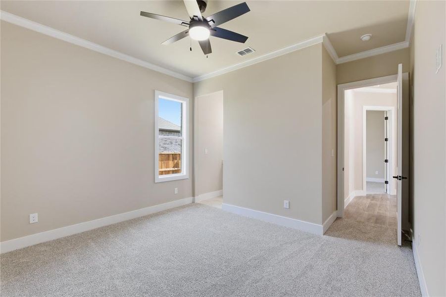 Spacious room with light neutral wall tones, plush gray carpeting, and crisp white baseboards and crown molding