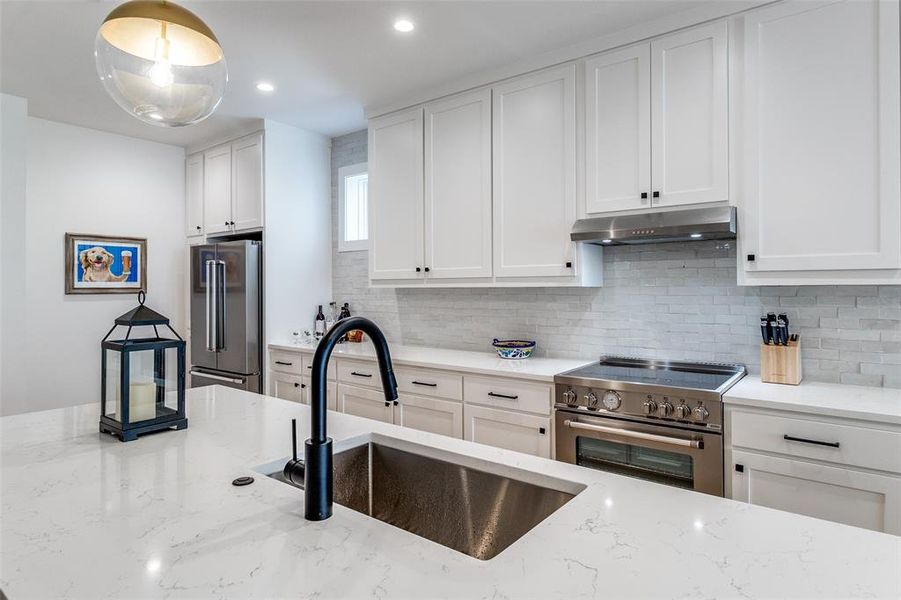 Kitchen featuring white cabinetry, high end appliances, decorative backsplash, light stone countertops, and recessed lighting Kitchen featuring white cabinetry, high end appliances, decorative backsplash, light stone countertops, and recessed lighting