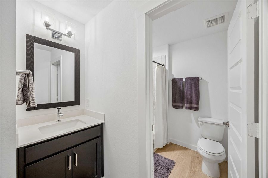 Stylish glass and chrome vanity light fixtures replacing builder-grade lighting, as well as wood-framed mirror.  There is a tub with a shower.