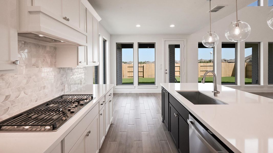 Kitchen featuring light countertops, appliances with stainless steel finishes, white cabinets, under cabinet range hood, and decorative light fixtures