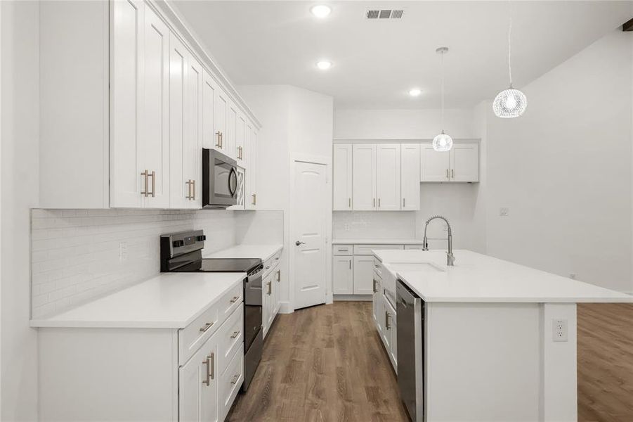 Kitchen with hanging light fixtures, stainless steel appliances, hardwood / wood-style floors, an island with sink, and white cabinets