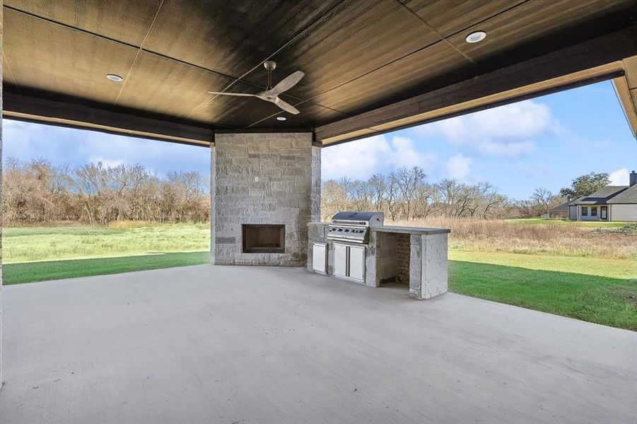 View of patio with an outdoor stone fireplace, grilling area, ceiling fan, and exterior kitchen