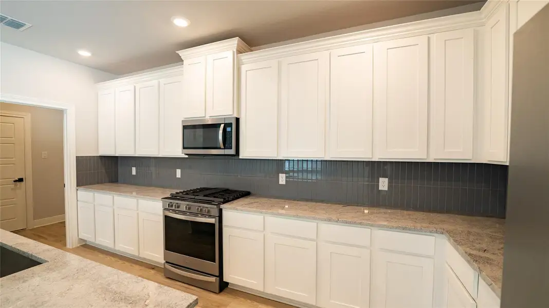 Kitchen with appliances with stainless steel finishes, white cabinetry, light stone countertops, light wood-style floors, and recessed lighting Kitchen with appliances with stainless steel finishes, white cabinetry, light stone countertops, light wood-style floors, and recessed lighting