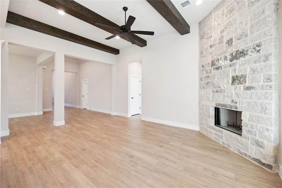 Unfurnished living room featuring beamed ceiling, ceiling fan, light hardwood / wood-style floors, and a fireplace