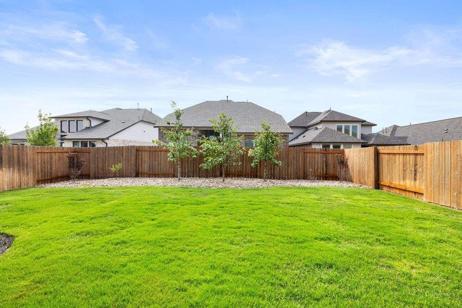 A sprawling lawn offers generous space for outdoor activities, fully enclosed by a robust wood fence.