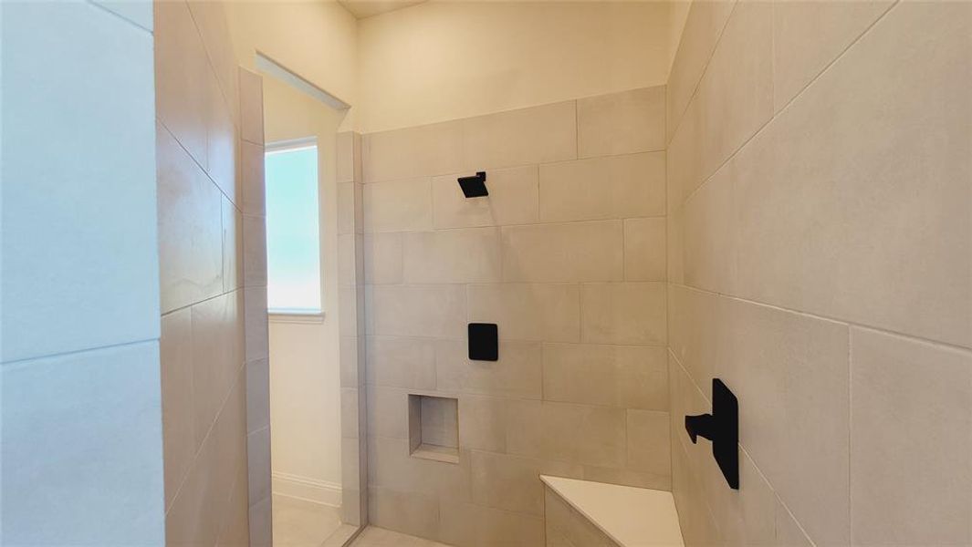 Spacious shower with large format tile walls, built-in bench seating, recessed shelf, and matte black fixtures