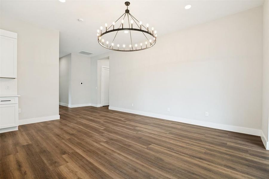 Spacious room featuring wood-finish flooring, a contemporary chandelier, recessed lighting, white baseboards, and neutral wall tones