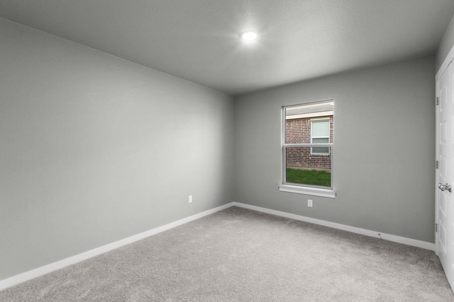 A well-lit bedroom features plush carpeting and a bright window overlooking the exterior.