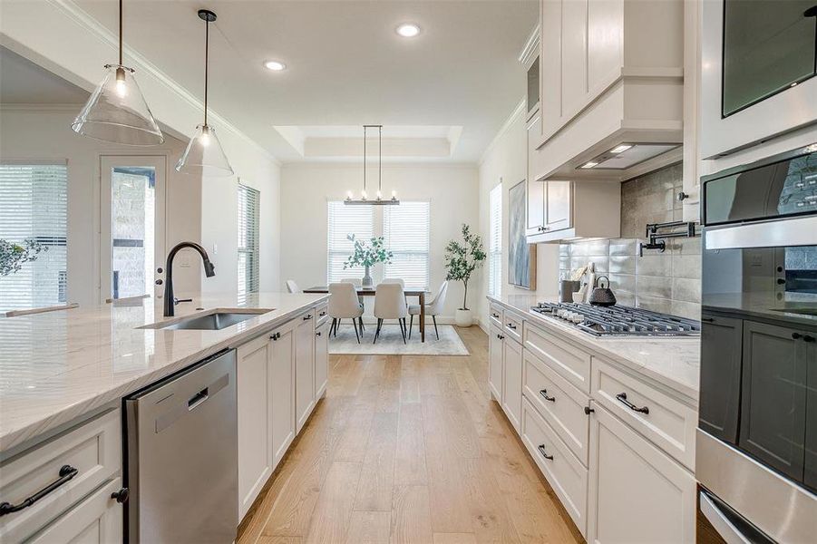 Kitchen with white cabinets, hanging light fixtures, stainless steel appliances, and light wood-type flooring