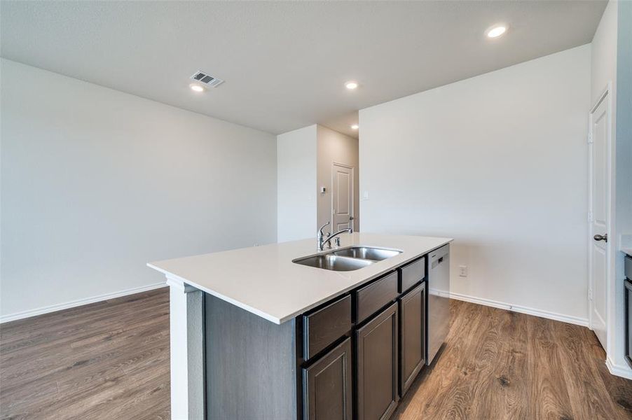 Kitchen featuring a kitchen island with sink, sink, stainless steel dishwasher, dark hardwood / wood-style floors, and dark brown cabinets