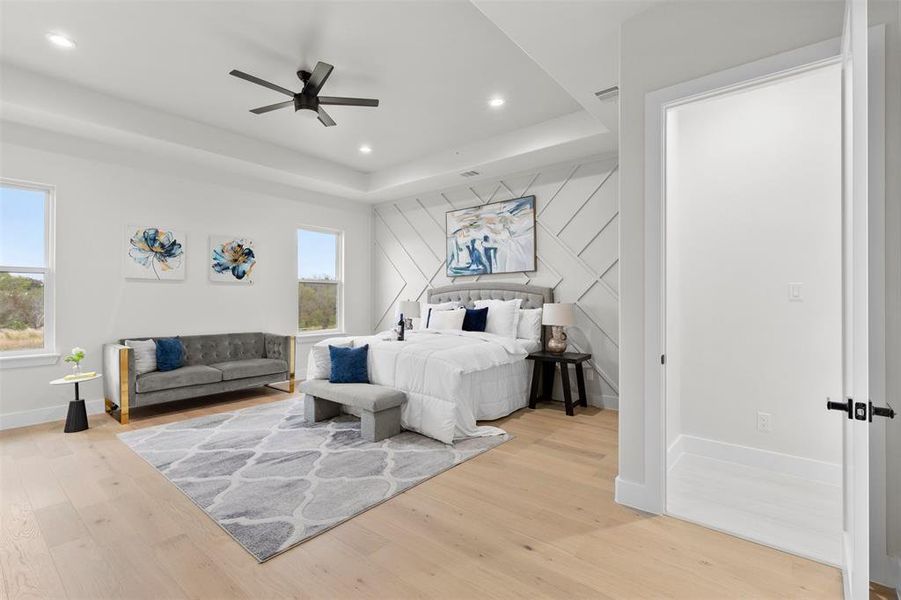 Bedroom with light wood-type flooring, ceiling fan, and a raised ceiling