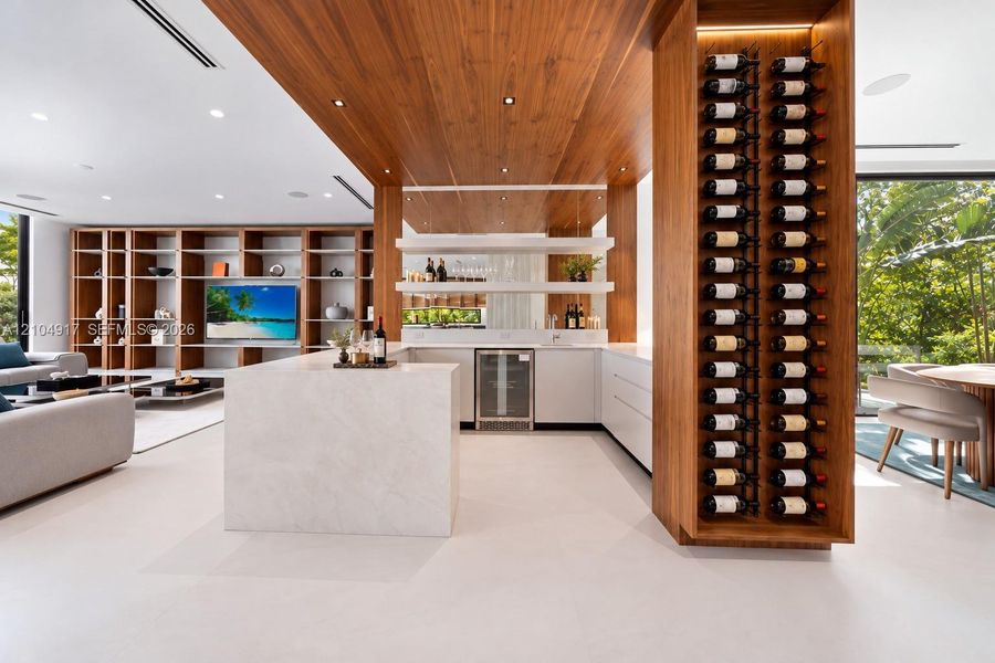 Custom wood-paneled ceiling, floor-to-ceiling built-in wooden shelving, integrated wine storage, waterfall-edge countertop, and inset beverage refrigerator