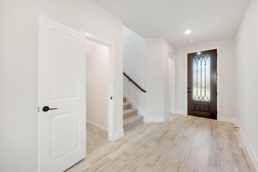 Entryway with wood front door with glass panels, light hardwood floors, and staircase with wood railing Entryway with wood front door with glass panels, light hardwood floors, and staircase with wood railing