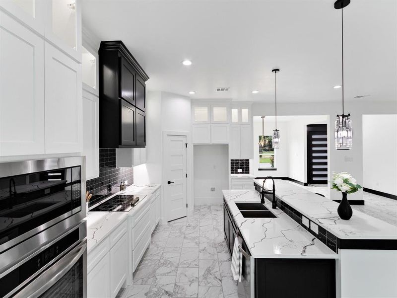Modern kitchen featuring an expansive center island with dual sinks, white countertops, black cabinetry, and stainless steel appliances