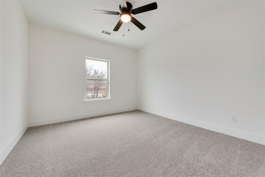 Spare room featuring carpet floors, baseboards, visible vents, and ceiling fan