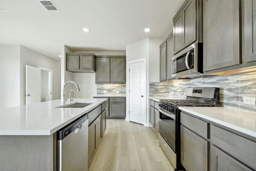 Kitchen featuring backsplash, a center island with sink, light hardwood / wood-style floors, sink, and stainless steel appliances