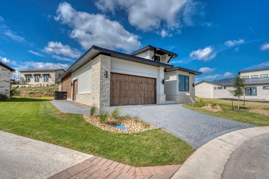 Textured stone veneer accents the exterior facade of this modern two-story home with paver driveway. Textured stone veneer accents the exterior facade of this modern two-story home with paver driveway.