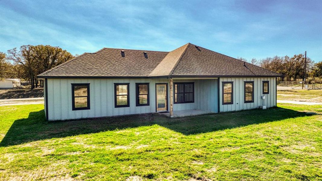 Back of property featuring a patio area, a yard, a shingled roof, and board and batten siding