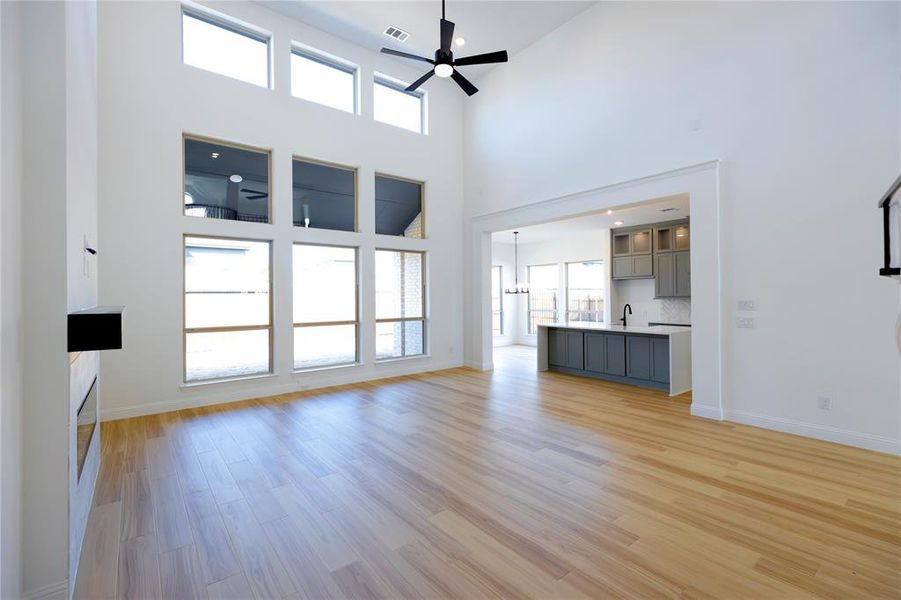 Unfurnished living room with light wood-type flooring, a ceiling fan, a high ceiling, a tile fireplace, and a chandelier Unfurnished living room with light wood-type flooring, a ceiling fan, a high ceiling, a tile fireplace, and a chandelier