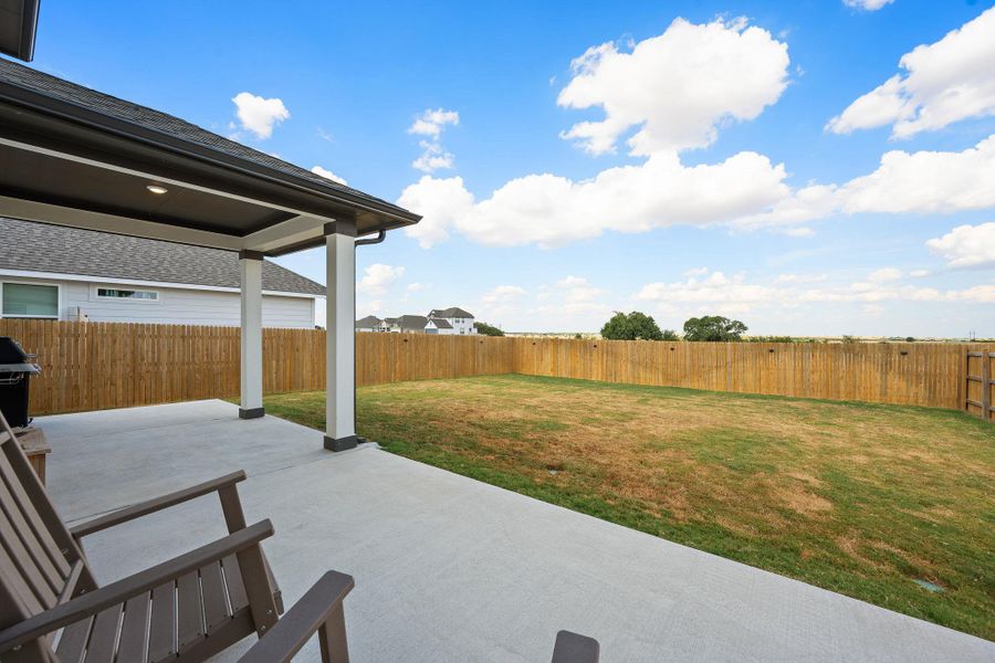 A spacious covered patio overlooks the fully fenced grassy backyard under open blue skies. A spacious covered patio overlooks the fully fenced grassy backyard under open blue skies.