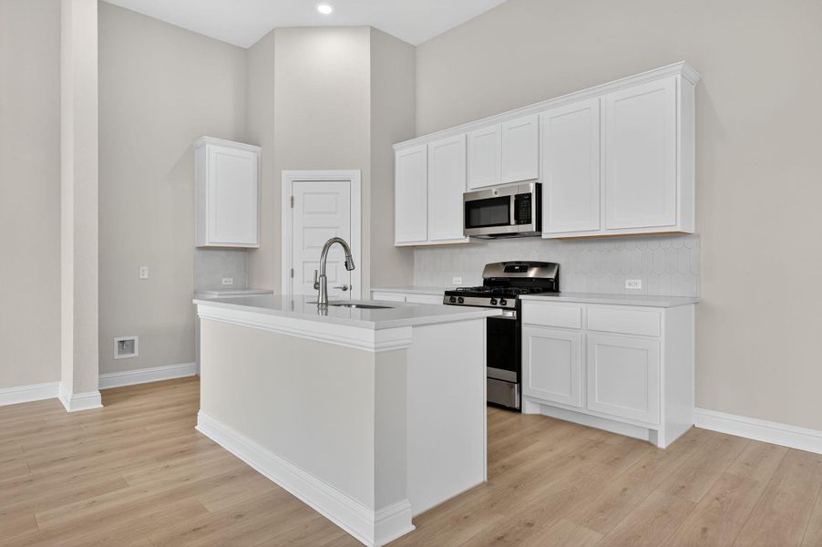 Kitchen featuring white cabinets, stainless steel appliances, an island with sink, light wood-style flooring, and a high ceiling