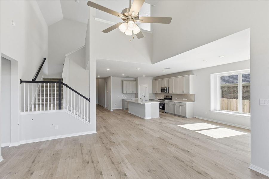 Unfurnished living room featuring high vaulted ceiling, stairs, light wood-style floors, and a ceiling fan Unfurnished living room featuring high vaulted ceiling, stairs, light wood-style floors, and a ceiling fan