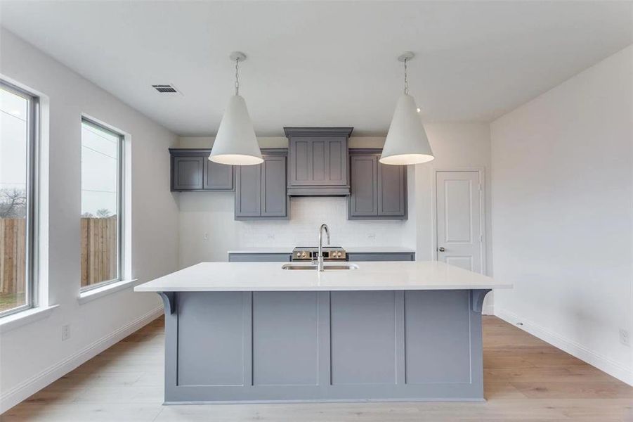 Kitchen with a sink, light countertops, decorative backsplash, a kitchen island with sink, and light wood-type flooring