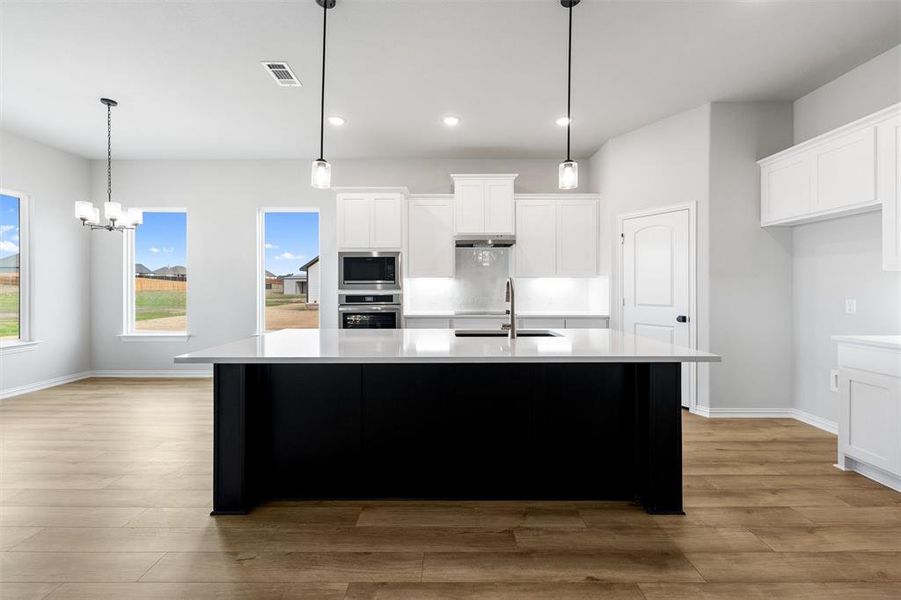 Kitchen with white cabinetry, a center island with sink, decorative light fixtures, appliances with stainless steel finishes, and recessed lighting Kitchen with white cabinetry, a center island with sink, decorative light fixtures, appliances with stainless steel finishes, and recessed lighting