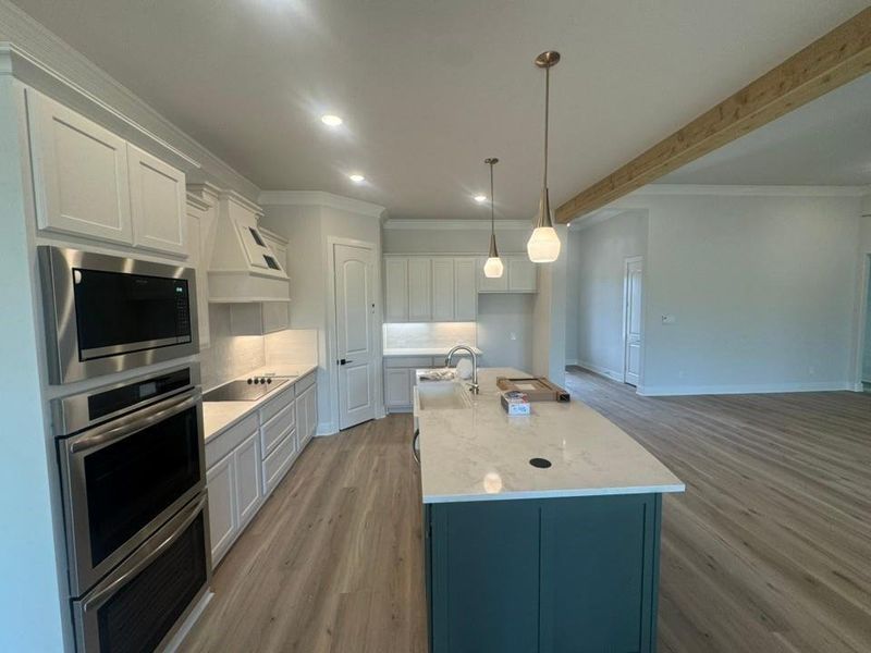Kitchen featuring light-finish cabinetry, stainless steel appliances, a center island with a contrasting finish, pendant lighting, and wood-finish flooring Kitchen featuring light-finish cabinetry, stainless steel appliances, a center island with a contrasting finish, pendant lighting, and wood-finish flooring