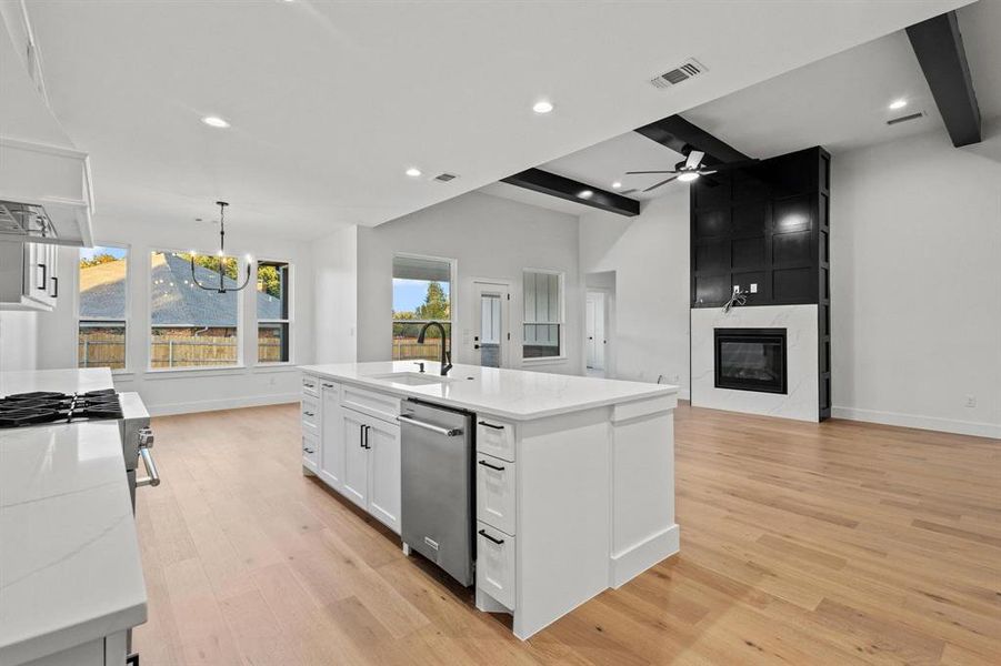 Kitchen with open floor plan, an island with sink, white cabinetry, beam ceiling, and light wood-type flooring