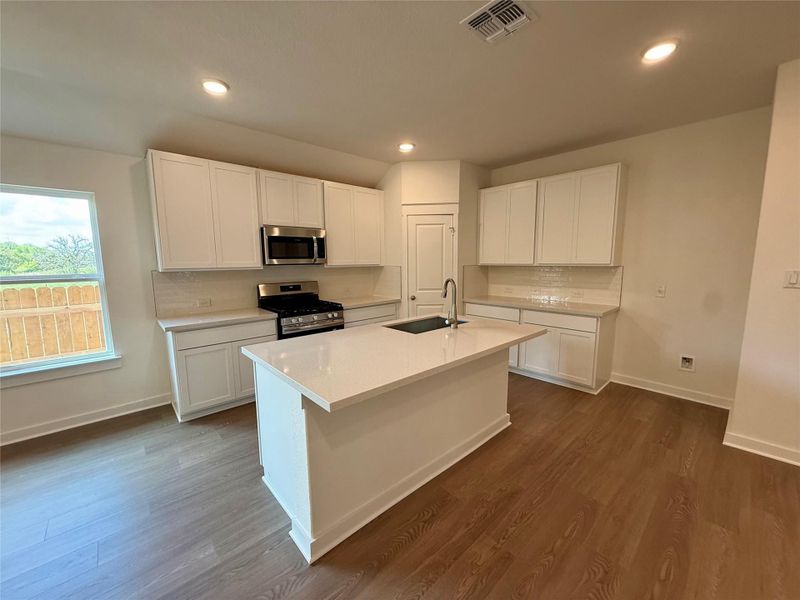 Kitchen featuring white cabinetry, stainless steel appliances, an island with sink, tasteful backsplash, and dark wood-style floors Kitchen featuring white cabinetry, stainless steel appliances, an island with sink, tasteful backsplash, and dark wood-style floors
