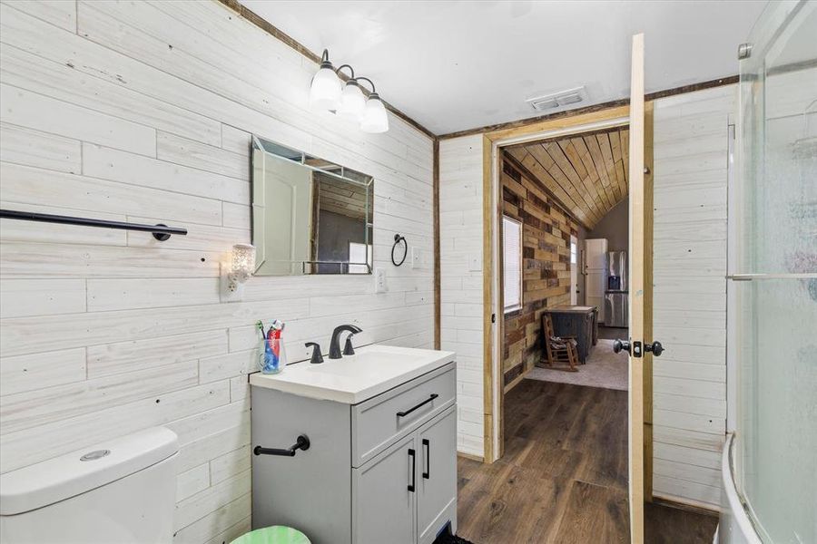 Full bathroom featuring wooden walls, vanity, dark wood-type flooring, and an enclosed shower