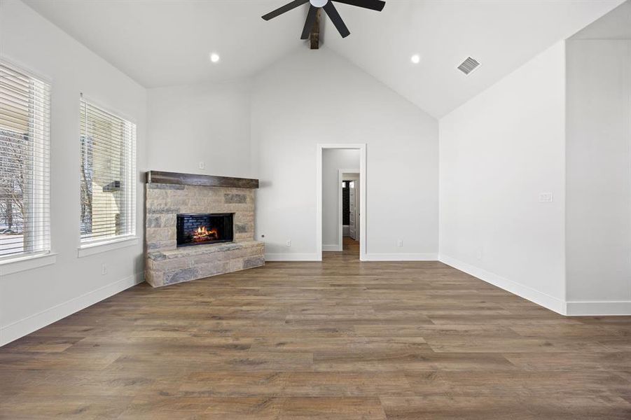 Unfurnished living room with a stone fireplace, dark wood-style flooring, a high ceiling, a ceiling fan, and recessed lighting