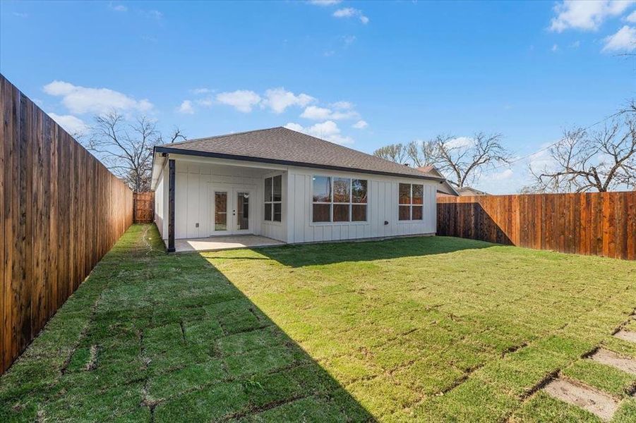 Rear view of house featuring a fenced backyard, a shingled roof, a yard, french doors, and board and batten siding