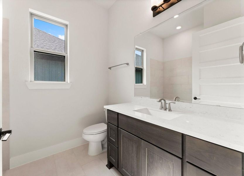 The secondary bathroom features dark wood cabinetry & light countertops. It includes a window for natural light and is styled with a neutral color palette.