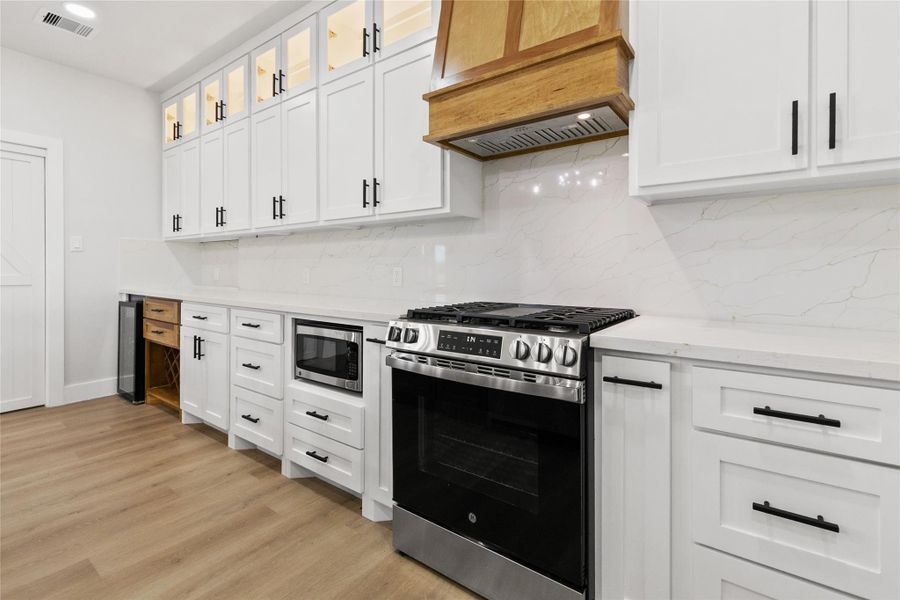 The kitchen blends style and function with quartz countertops, a wood island with an apron-front farmhouse sink, beverage refrigerator, wine storage, under-counter microwave, lighted glass-front cabinetry, and a large walk-in pantry.