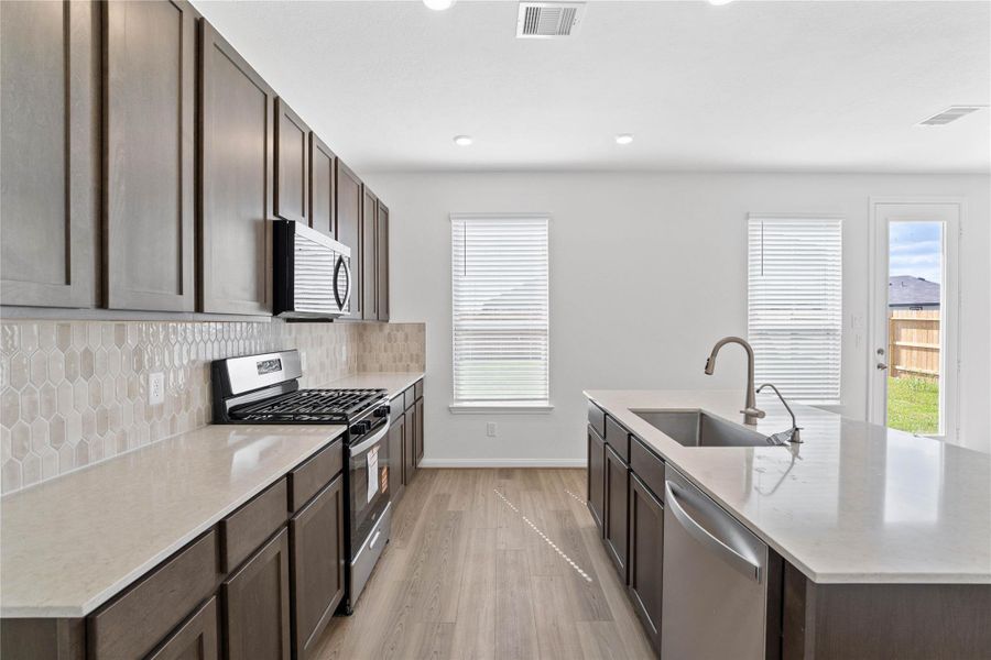 This spacious kitchen boasts soaring ceilings, Woodmont Dakota cabinets in a Smolder stain, Silestone Lagoon countertops, stainless steel Whirlpool appliances, a modern Daltile picket backsplash, recessed lighting, an extended breakfast bar countertop, and a pantry—all overlooking the expansive Gamily Room. This spacious kitchen boasts soaring ceilings, Woodmont Dakota cabinets in a Smolder stain, Silestone Lagoon countertops, stainless steel Whirlpool appliances, a modern Daltile picket backsplash, recessed lighting, an extended breakfast bar countertop, and a pantry—all overlooking the expansive Gamily Room.