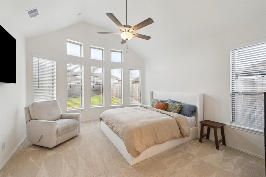 Tucked at the back of the home for privacy, the primary suite is a true retreat, featuring tall ceilings, elongated windows that flood the room with natural light, and a ceiling fan for year-round comfort.
