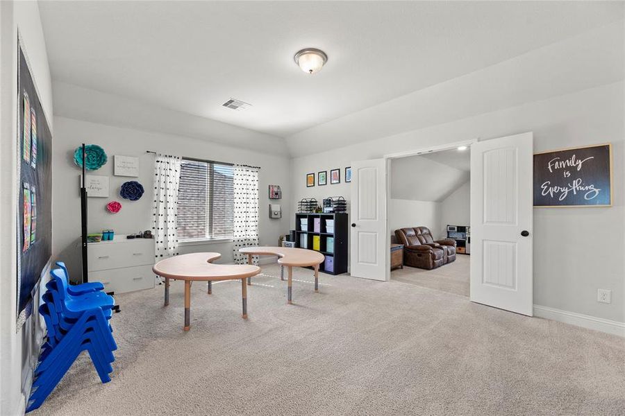 This is a spacious, well-lit room with neutral color carpeting.There are two open doorways leading to adjoining rooms, one displaying a cozy seating area.