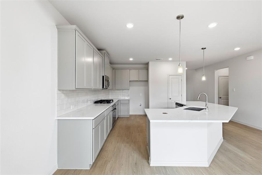 Kitchen featuring an island with sink, light wood-style flooring, hanging light fixtures, light stone counters, and tasteful backsplash