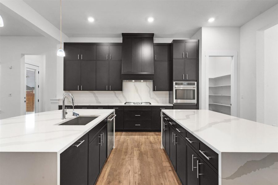 Kitchen featuring a large island, dark cabinets, pendant lighting, light stone countertops, and recessed lighting