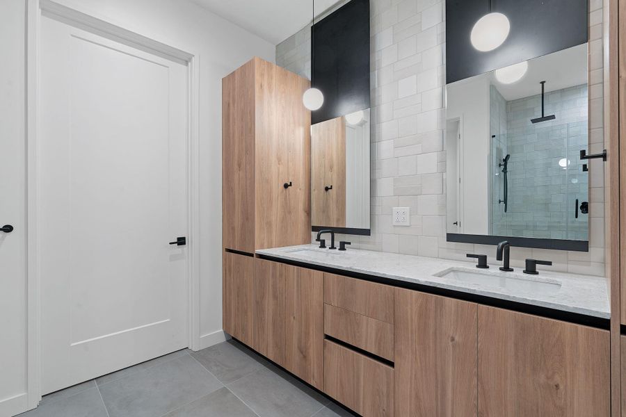 Bathroom featuring a stall shower, double vanity, light tile patterned floors, and tasteful backsplash