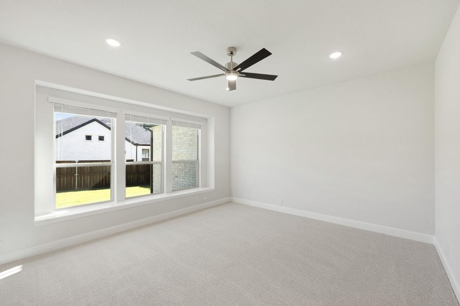Empty bedroom with carpet flooring, ceiling fan, and large window overlooking backyard
