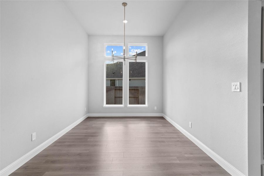 This breakfast/dining room is defined by its soaring ceilings and a modern chandelier, with large windows that bathe the neutral-toned space in natural light.