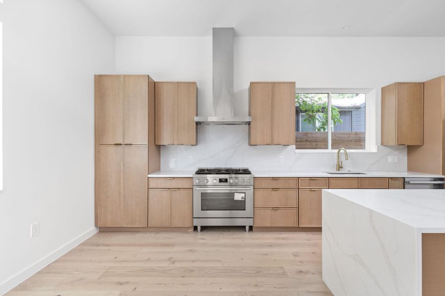 Kitchen with stainless steel range with gas stovetop, wall chimney exhaust hood, light wood finished floors, and modern cabinets Kitchen with stainless steel range with gas stovetop, wall chimney exhaust hood, light wood finished floors, and modern cabinets