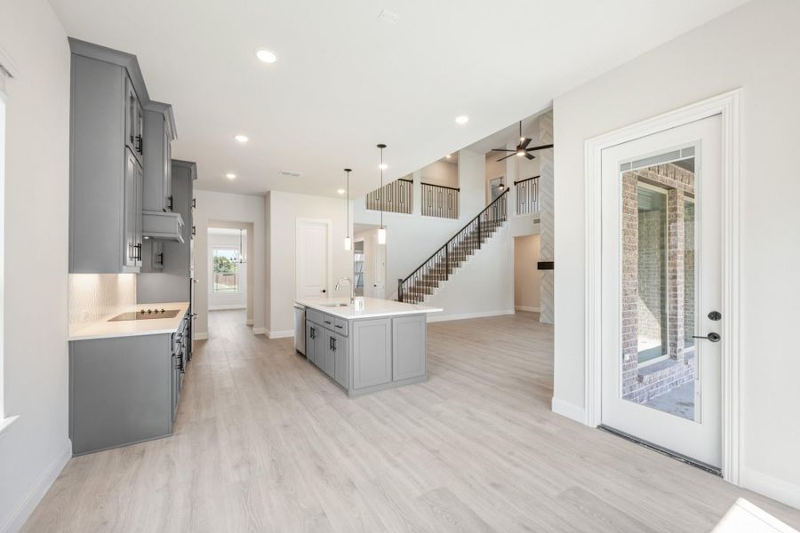 Open-concept kitchen with gray cabinets, center island, and staircase visible in background on light wood floors