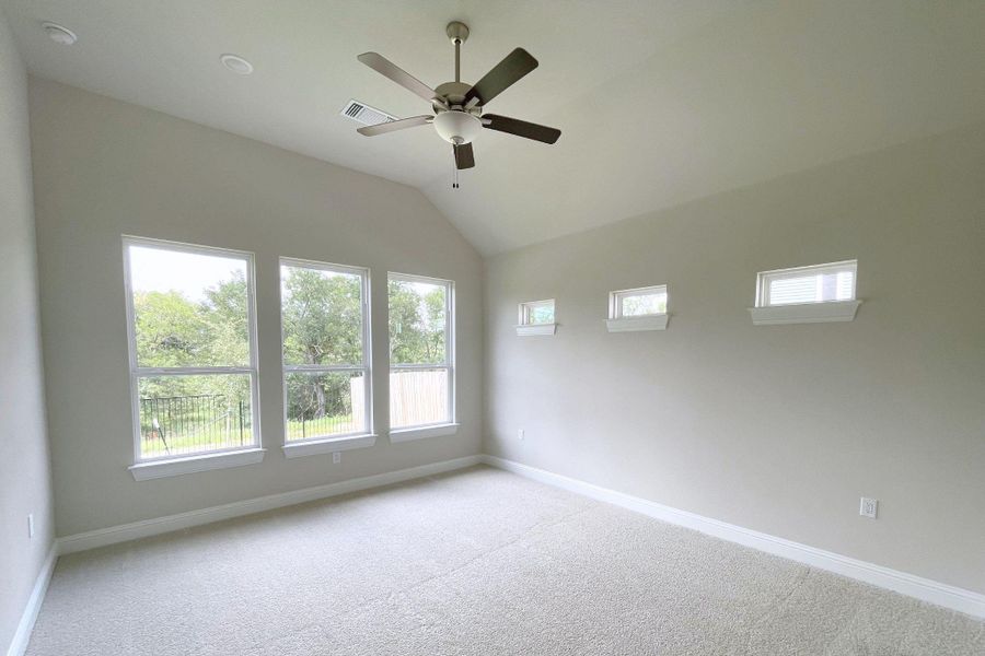 A spacious bedroom featuring high vaulted ceilings and ample natural light from multiple large windows.
