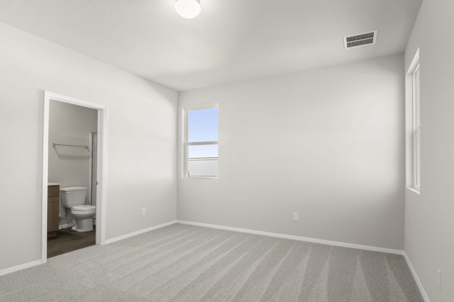 Image of a primary bedroom with tan carpeting and cream colored walls and a door connecting to the primary bathroom