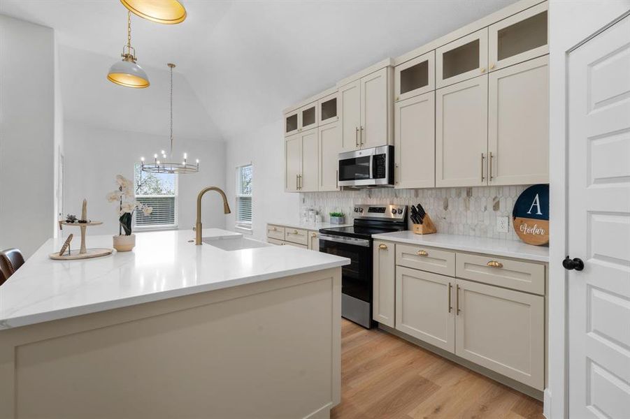 Kitchen with pendant lighting, appliances with stainless steel finishes, tasteful backsplash, glass insert cabinets, and an island with sink